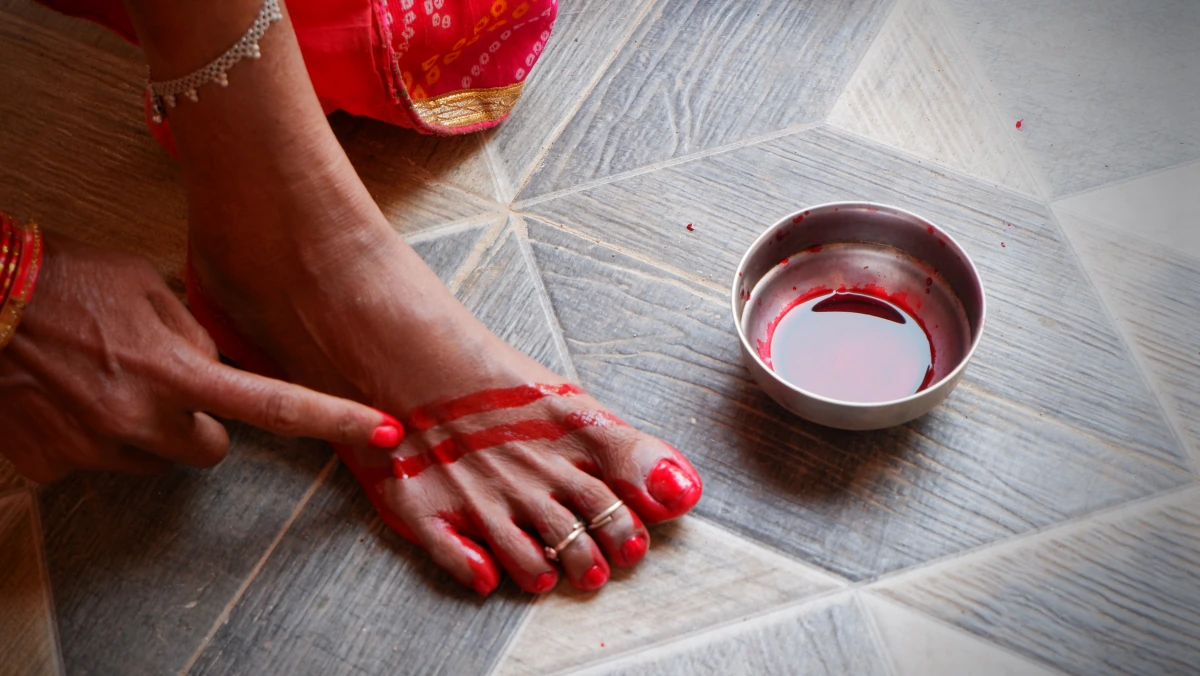 Red alta being painted around a woman's foot, with silver toe rings on her toes and a silver anklet above