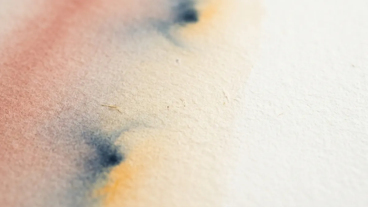 Handmade paper with a soft watercolour wash of earth red, indigo and ochre fading to cream