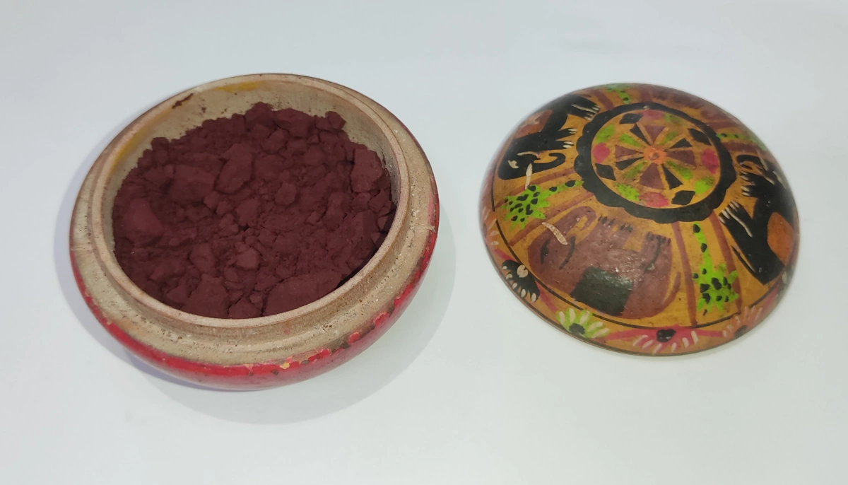 Dark red sindoor powder in an open wooden box beside its painted lid, the colour worn in the hair parting